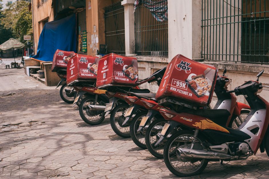 Motorbikes with branded delivery boxes parked on an urban sidewalk, showcasing food delivery services.
