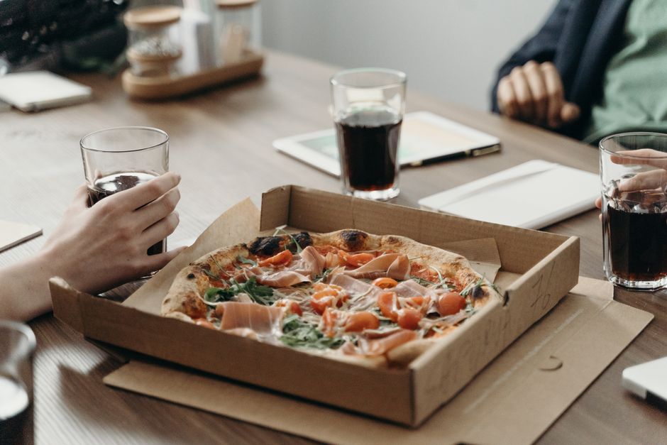 Office colleagues sharing a pizza and drinks during a casual lunch meeting.