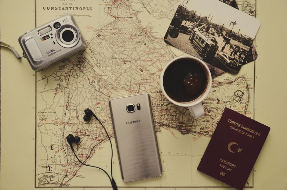Flat lay of travel essentials including a map, passport, coffee, and gadgets on a desk.